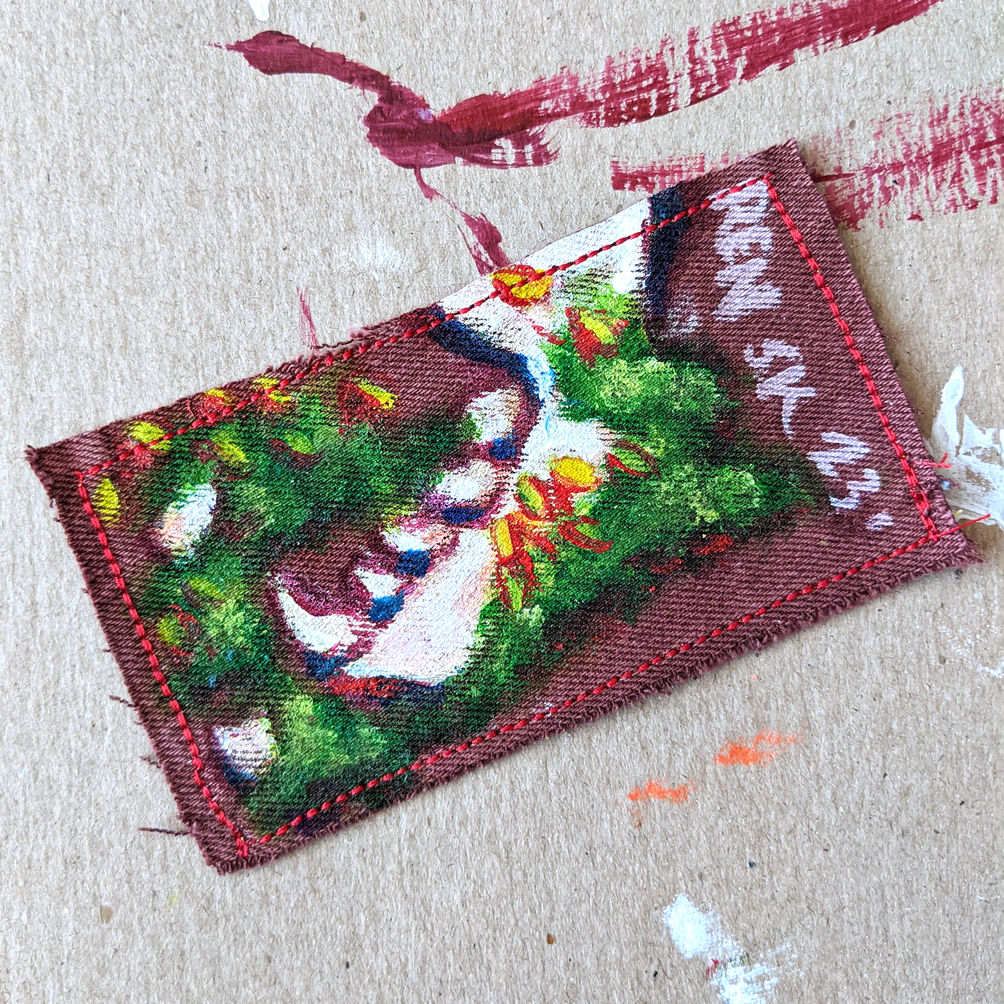 Hand painted patch of a raccoon jaw bone and teeth in flowering moss on rust colored denim.