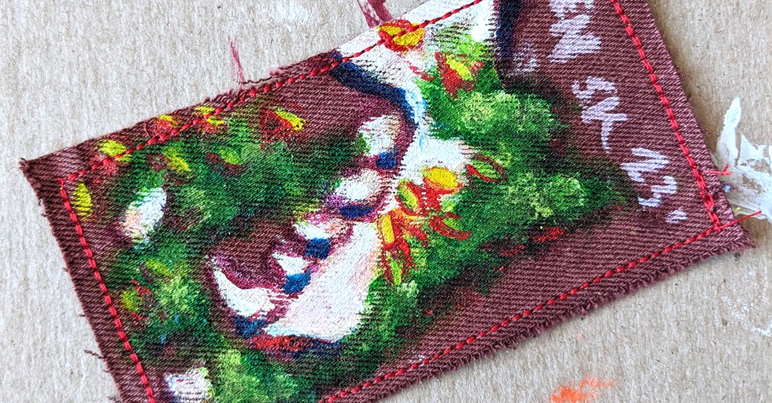 Hand painted patch of a raccoon jaw bone and teeth in flowering moss on rust colored denim.