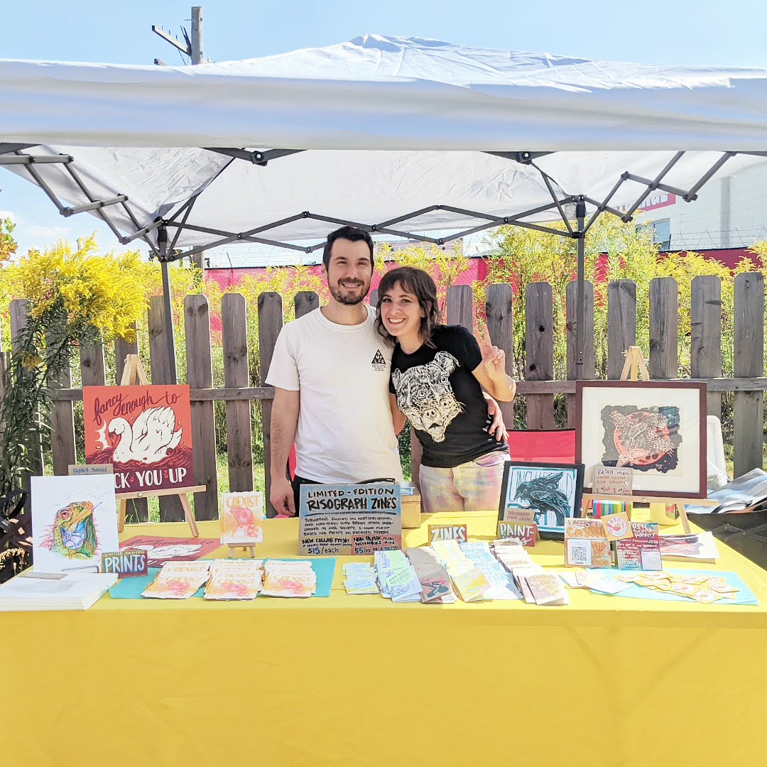 Mark and I tabling Gluestick Zine Fest at Black Circle Market last September behind a table with a yellow cloth.