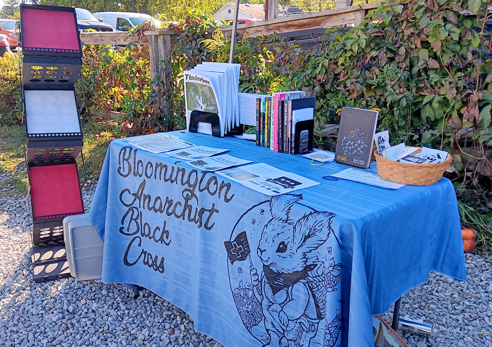 Photo of a distro table with blue tablecloth, rabbit logo and pamphlets and books 